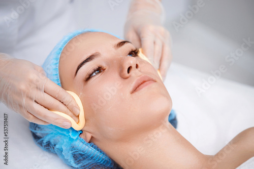 beautician cleanses skin of beautiful woman with a sponge.