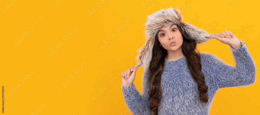 funny child in sweater and earflap hat on yellow background, winter. Banner of child girl in winter hat, studio poster header with copy space. funny child in sweater and earflap hat on yellow background, winter. Banner of child girl in winter hat, studio poster header with copy space.