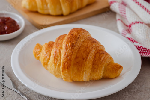 Fresh croissant on white plate and jam on table.