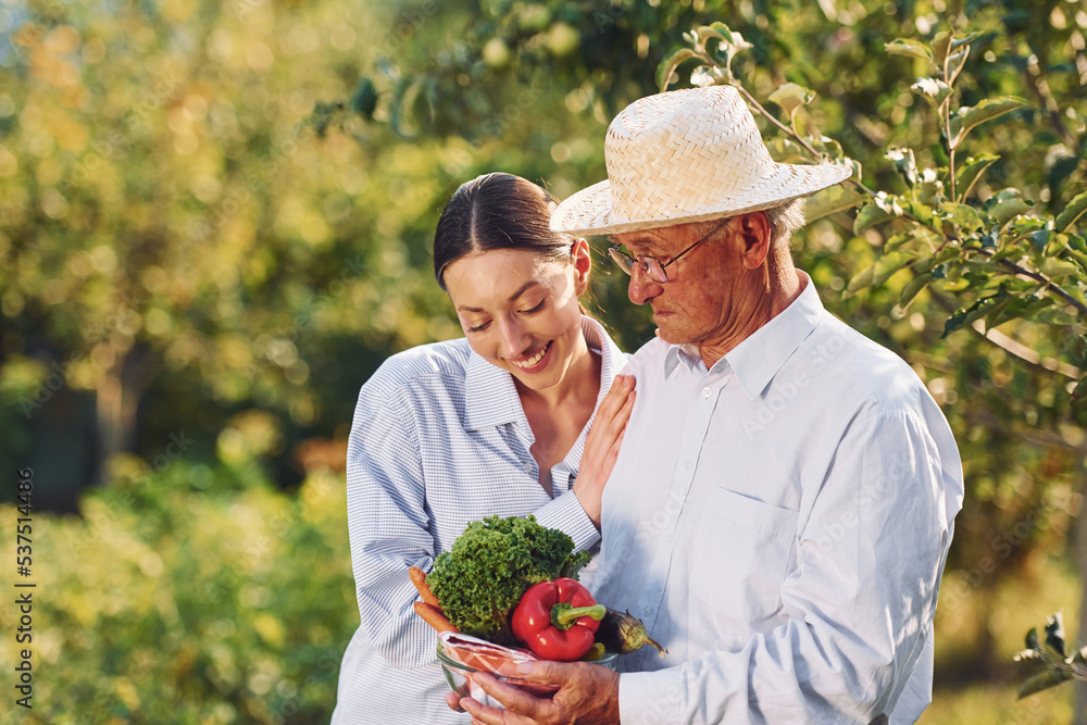 With vegetables in hands. Daughter is with her senior father in the garden at daytime With vegetables in hands. Daughter is with her senior father in the garden at daytime