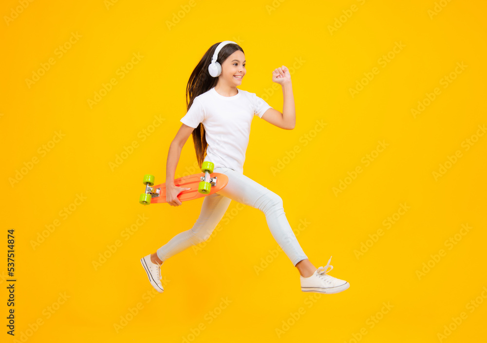 Teen girl 12, 13, 14 years old with skateboard over studio background. Jump and run. Cool modern teenager in stylish clothes. Teenagers lifestyle, casual youth culture. Happy teenager portrait.