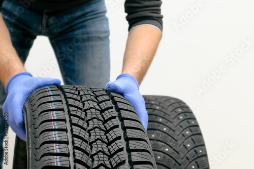 Replacement of winter and summer tires. Mechanic holding a tire at the white background. winter studded tyre, tires replacement © Trik