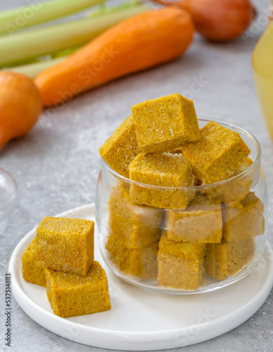 Homemade vegetable bouillon cubes made of braised onion, carrot, celery sticks and salt served in glass jar with ingredients on background. Vertical, selective focus.