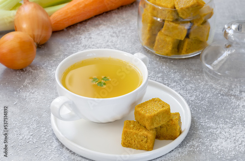 Homemade vegetable cubes with ready to eat bouillon in a bowl and ingredients on background. photo