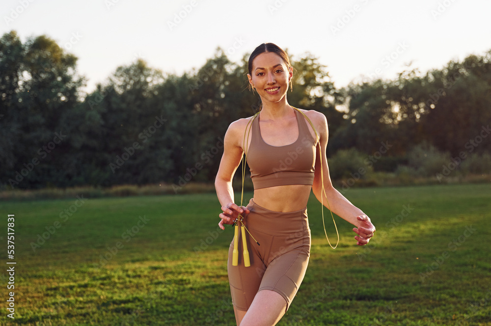 Holding jumping ropes. Young woman in yoga clothes is outdoors on the field Holding jumping ropes. Young woman in yoga clothes is outdoors on the field