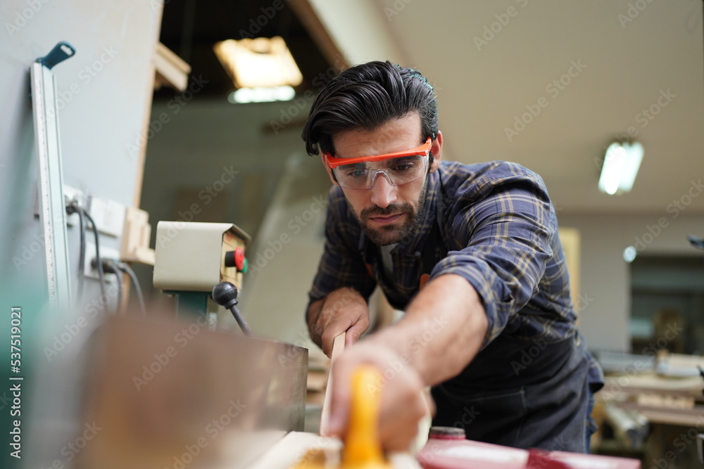 Contemporary Carpenter Working, Portrait of modern carpenter making wood furniture while working in joinery lit by sunlight with factory background on small business concept, copy space Contemporary Carpenter Working, Portrait of modern carpenter making wood furniture while working in joinery lit by sunlight with factory background on small business concept, copy space