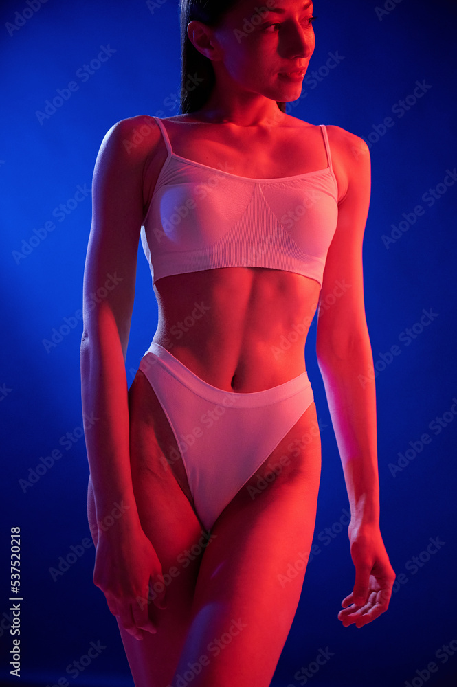 Illuminated by red color. Young woman in underwear is in the studio with neon lights Illuminated by red color. Young woman in underwear is in the studio with neon lights