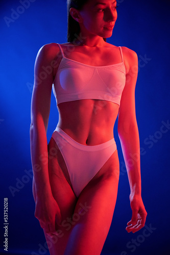 Illuminated by red color. Young woman in underwear is in the studio with neon lights