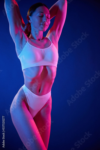 Slim body type. Young woman in underwear is in the studio with neon lights