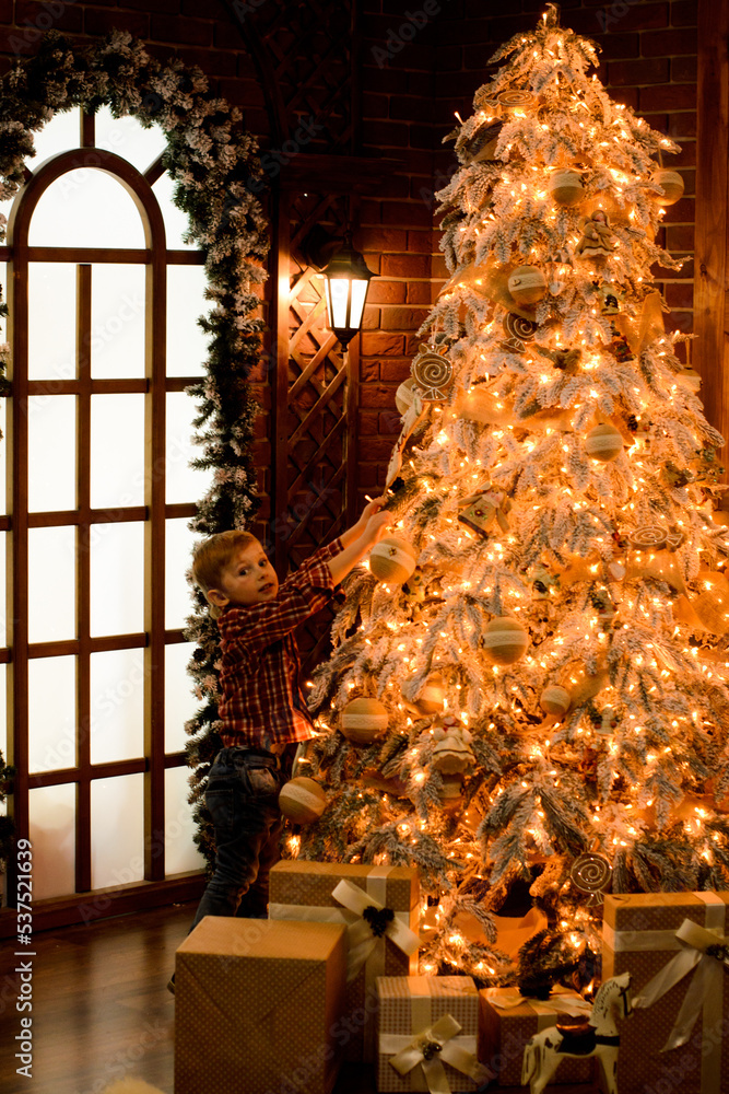 Christmas tree magically glows with New Year's orange lights, a little boy decorates it