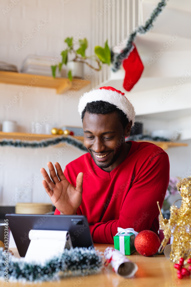 Happy african american man wearing santa hat, using tablet for video call