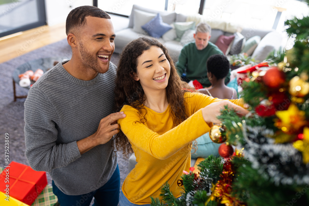 Image of happy diverse couple celebrating christmas at home decorating the tree