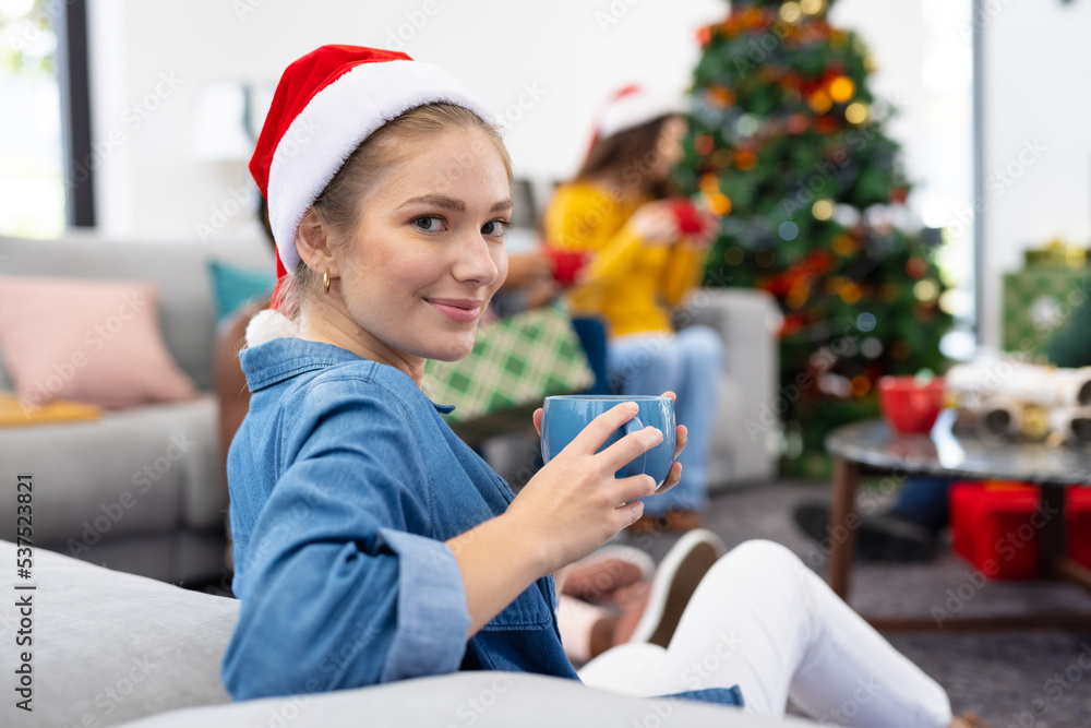 Image of smiling caucasian woman holding mug, celebrating christmas at home with friends Image of smiling caucasian woman holding mug, celebrating christmas at home with friends
