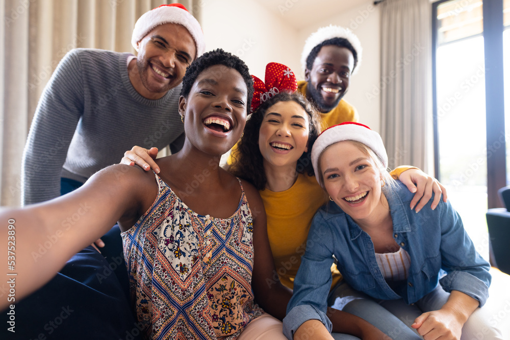 Image of happy diverse friends celebrating christmas at home taking selfie