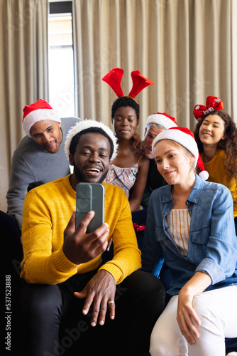 Vertical image of happy diverse friends celebrating christmas at home making smartphone video call