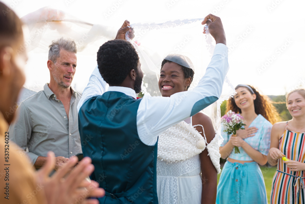 Happy african american couple holding veil and smiling during wedding