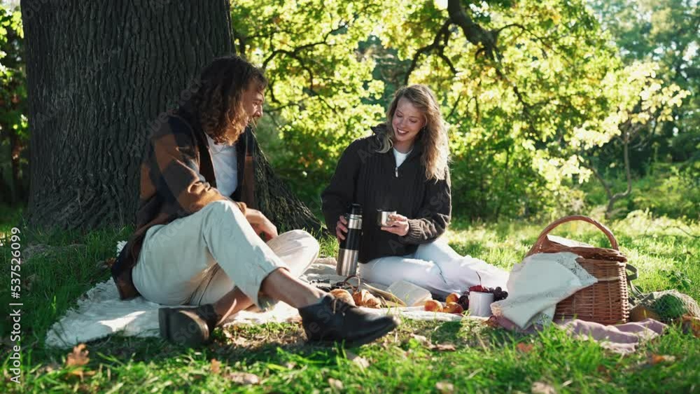 Smiling young couple drinking hot tea and talking at a picnic in the park outdoors Smiling young couple drinking hot tea and talking at a picnic in the park outdoors