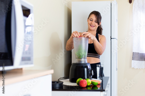 Young happy woman in the home kitchen preparing a detox juice in the blender.