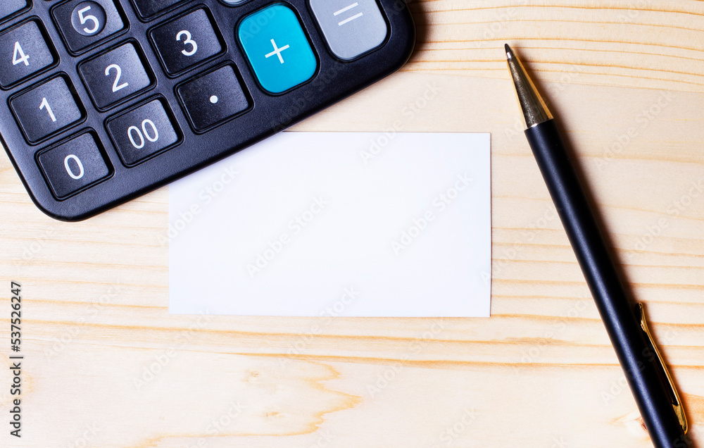 On a wooden table, a pen, a calculator and an empty business card with a place to insert text On a wooden table, a pen, a calculator and an empty business card with a place to insert text