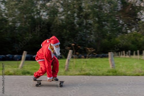 caucasian man dressed as santa claus skating on a longboard skateboard on a country road. christmas and sport concept.