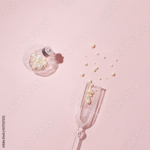 Champagne glass and beads as bubbles, minimal creative concept on a pastel pink background. Merry Christmas and Happy New Year greeting card. Girly fashion style. 