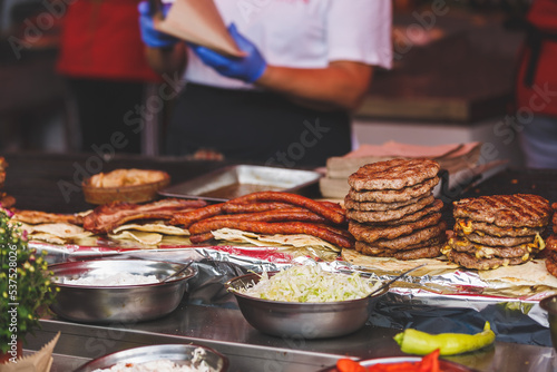 Street Food- grilled sausage and meat  at a food stand,  serbian burger, called pljeskavica and saussages. Appetizing sausages and meat on big grill in outdoors market in Serbia. Selective focus photo