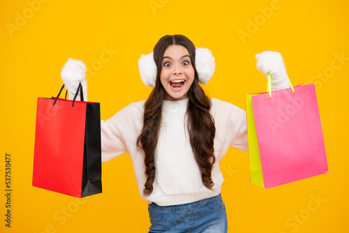 Child girl hold shopping bag enjoying sale isolated on yellow background. Winter shopping sale. Portrait of teenager girl is ready to go shopping. Excited teenager girl.