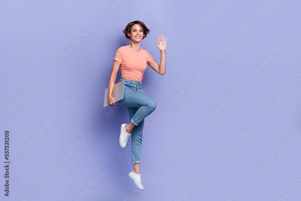 Full length photo of shiny friendly lady wear striped t-shirt jumping holding modern device waving arm empty space isolated violet color background Full length photo of shiny friendly lady wear striped t-shirt jumping holding modern device waving arm empty space isolated violet color background
