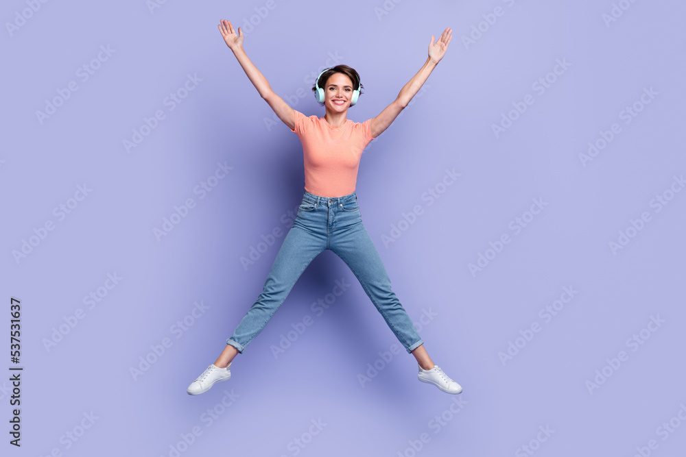 Full length photo of shiny adorable lady wear striped t-shirt earphones jumping high like star isolated violet color background