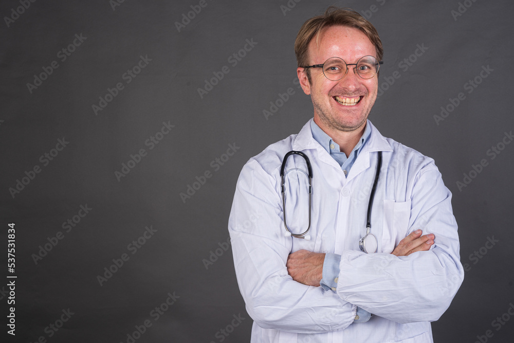 Confident male doctor smiling with arms crossed against gray background Confident male doctor smiling with arms crossed against gray background