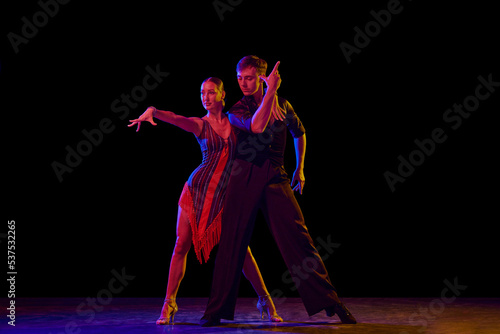 Stylish ballroom dancers couple in gorgeous outfits dancing in sensual pose on dark background in neon light. Concept of art, music, dance, emotions. © master1305