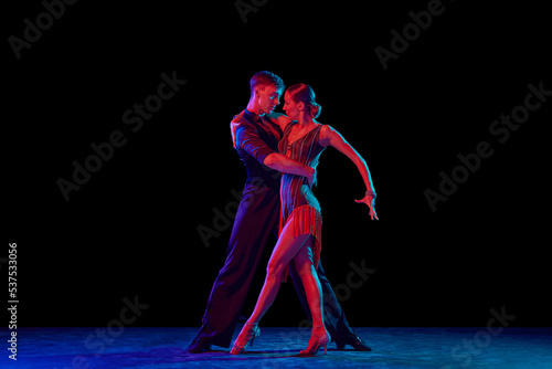 Billede på lærred Stylish ballroom dancers couple in gorgeous outfits dancing in sensual pose on dark background in neon light