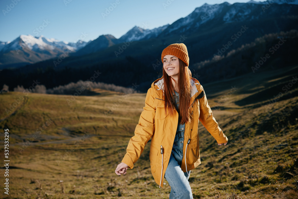 Woman standing beautifully on a hill smile with teeth in the mountains in the autumn in a yellow raincoat and jeans happy sunset trip to hike the mountains in the snow, freedom lifestyle 