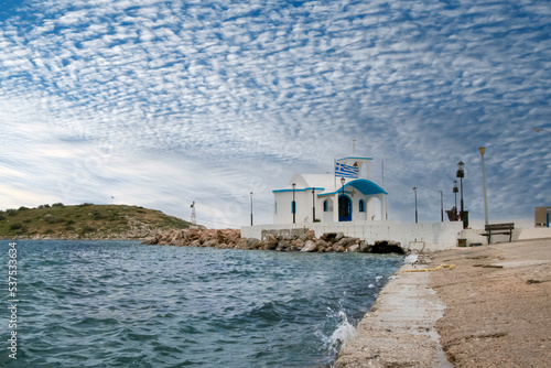 Greek white chapel over sea and small bay under a dramatic sky  photo