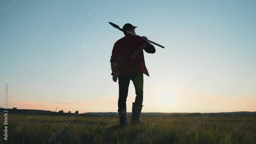 Agricultural business. Male farmer walking through a green field with shovel. Farmer-agronomist works in the field. Agricultural business. Male farmer walking through a green field with shovel. Farmer-agronomist works in the field.