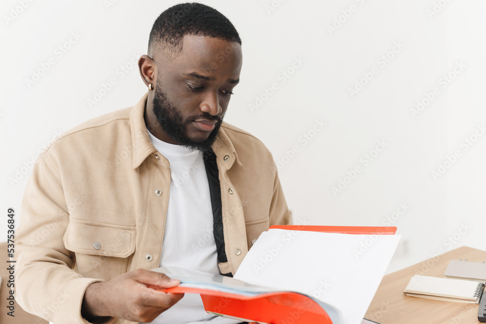 Problems in the household budget during the crisis. Young black sad man looking through mortgage papers or economic reports, upset and angry. Problems in the household budget during the crisis. Young black sad man looking through mortgage papers or economic reports, upset and angry.