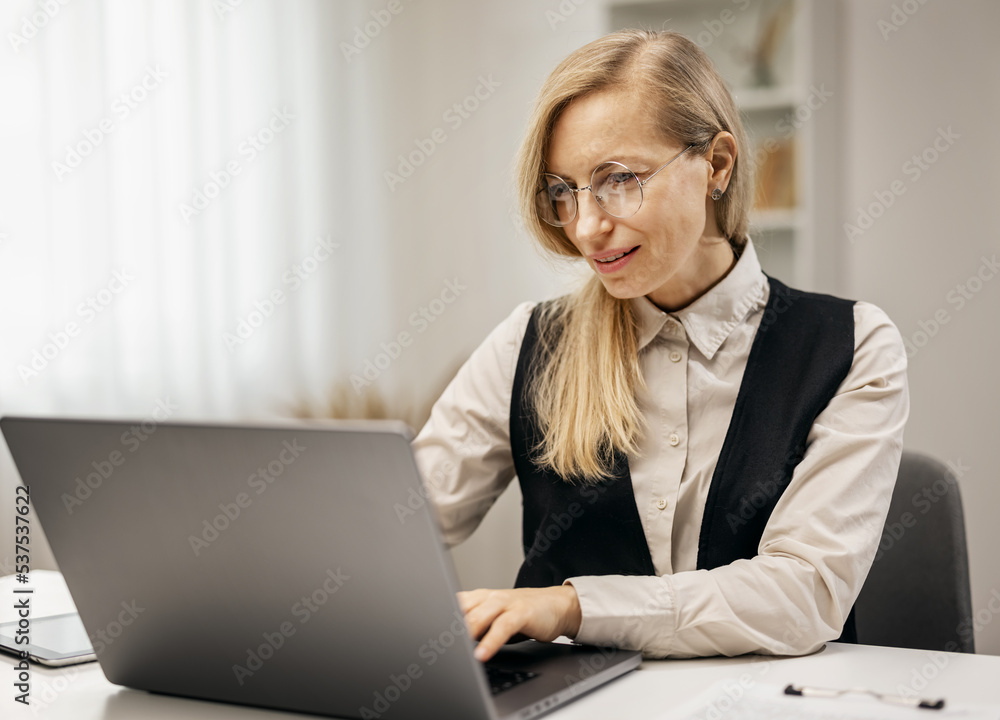 Mature blonde woman writer working with laptop at home, cheerful lady typing novel at desk Mature blonde woman writer working with laptop at home, cheerful lady typing novel at desk