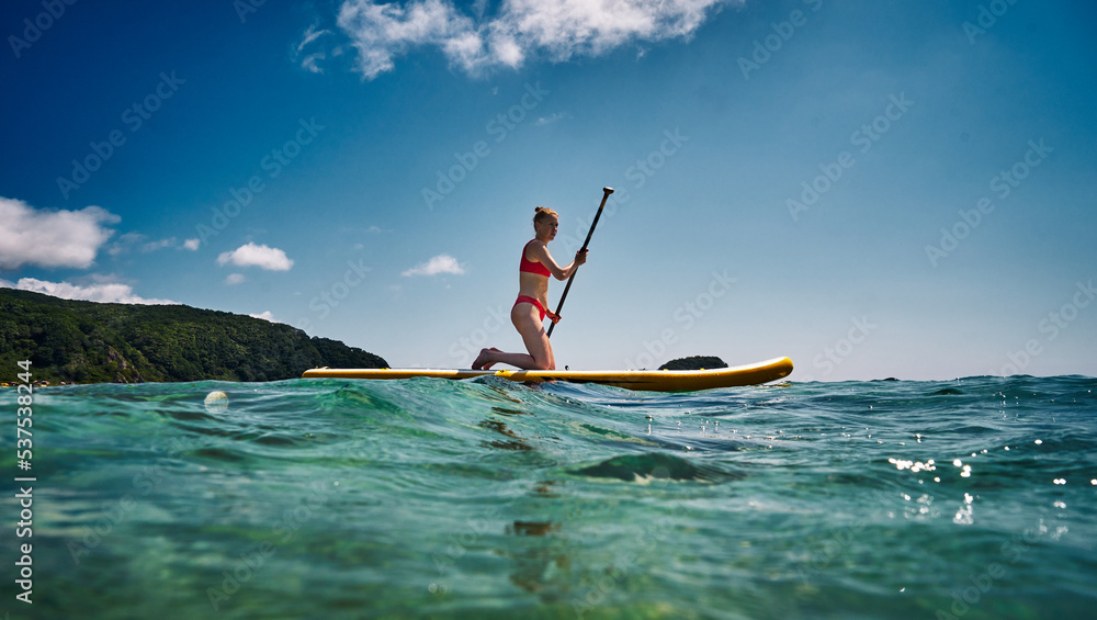 Tanned woman in red bikini sitting on surfboard with paddle relaxing at sea resort enjoying summer Tanned woman in red bikini sitting on surfboard with paddle relaxing at sea resort enjoying summer