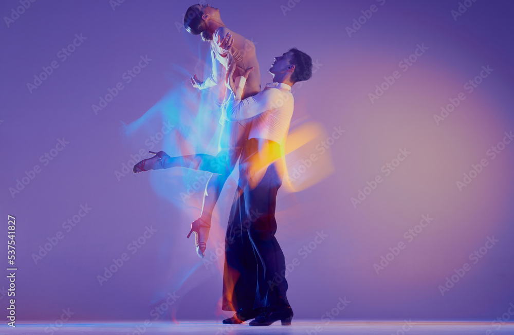Young graceful dancers, flexible man and woman dancing ballroom dance isolated on gradient blue purple background in neon mixed light. Young graceful dancers, flexible man and woman dancing ballroom dance isolated on gradient blue purple background in neon mixed light.