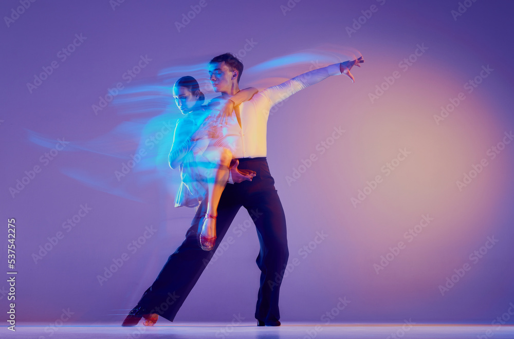 Young graceful dancers, flexible man and woman dancing ballroom dance isolated on gradient blue purple background in neon mixed light. Young graceful dancers, flexible man and woman dancing ballroom dance isolated on gradient blue purple background in neon mixed light.