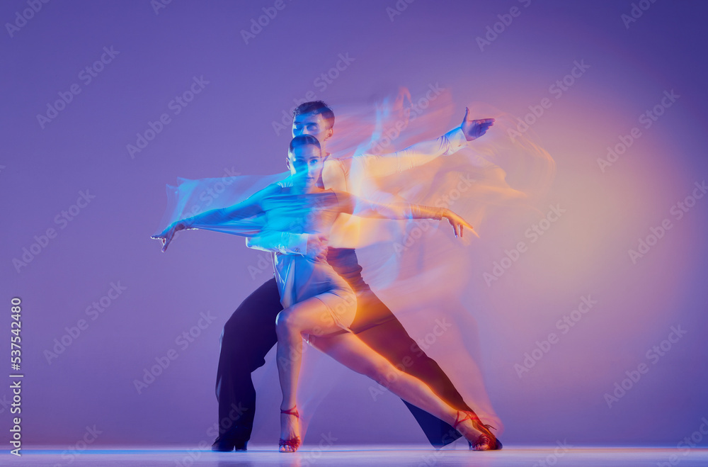 Art in motion. Flexible adorable ballroom dancers in stage attires dancing isolated on purple background in neon mixed light. Music, dance, emotions