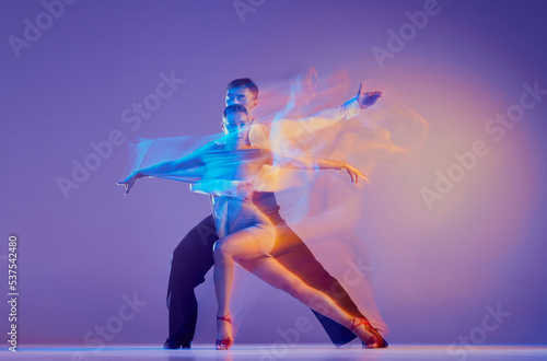 Art in motion. Flexible adorable ballroom dancers in stage attires dancing isolated on purple background in neon mixed light. Music, dance, emotions © master1305