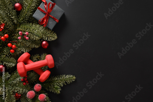 Fototapeta Naklejka Na Ścianę i Meble -  Christmas sport composition with gift and two red sports dumbbells on black background. Top view with copy space. Fitness, sport and healthy concept. Christmas greeting card. Winter sale.