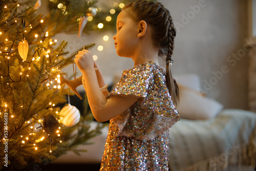 winter holidays and people concept - happy little girl decorating christmas tree at home.