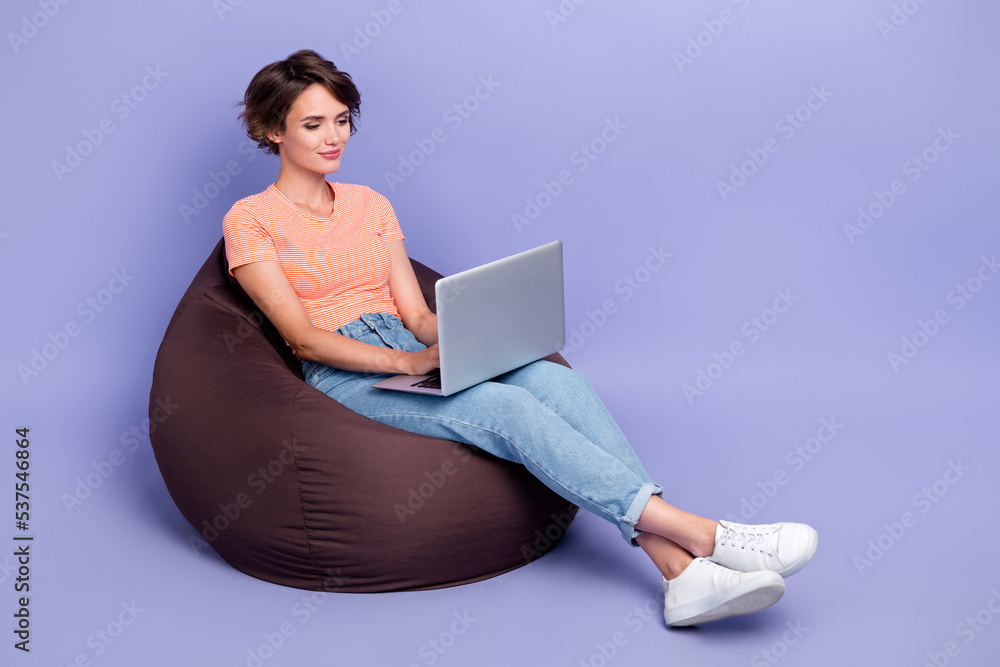 Naklejka premium Full body photo of pretty young girl work remotely laptop brown beanbag dressed stylish striped clothes isolated on purple color background