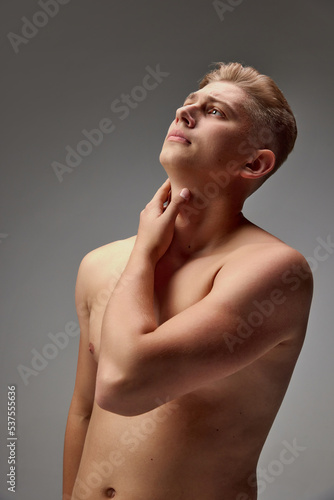 Portrait of young handsome man with blonde hair looking upwards, posing shirtless isolated over grey studio background. Sportive body