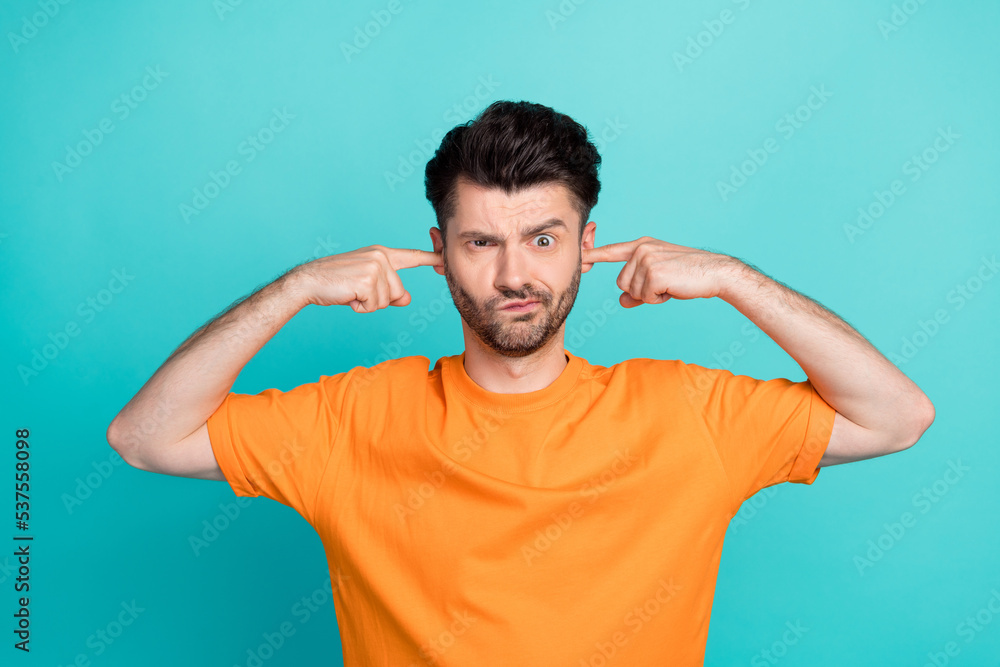 Closeup photo of young funny attractive handsome cute guy wear orange t-shirt put fingers ears pouted lips unhappy loud music grimace isolated on cyan color background Closeup photo of young funny attractive handsome cute guy wear orange t-shirt put fingers ears pouted lips unhappy loud music grimace isolated on cyan color background