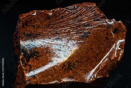 Real shiny specimen of orange Mahogany Obsidian volcanic stone macro isolated on black leather background