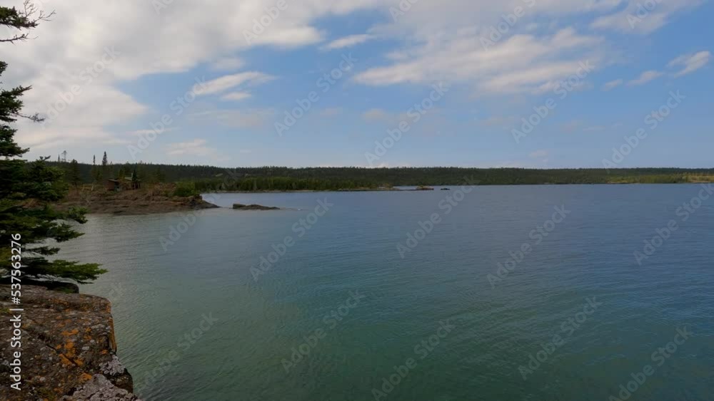 Spectacular Views of Lake Superior from the Coast of Isle Royale National Park. A coastline of green coniferous tress can be seen in the distance. Cloudy blue sky above. Spectacular Views of Lake Superior from the Coast of Isle Royale National Park. A coastline of green coniferous tress can be seen in the distance. Cloudy blue sky above.