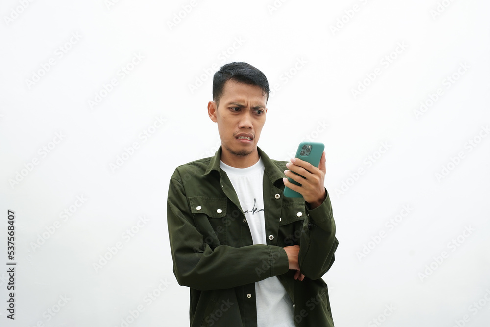 Asian man wearing casual green shirt looking at smartphone screen with shocked, surprised, dumbfounded expression. isolated white background Asian man wearing casual green shirt looking at smartphone screen with shocked, surprised, dumbfounded expression. isolated white background